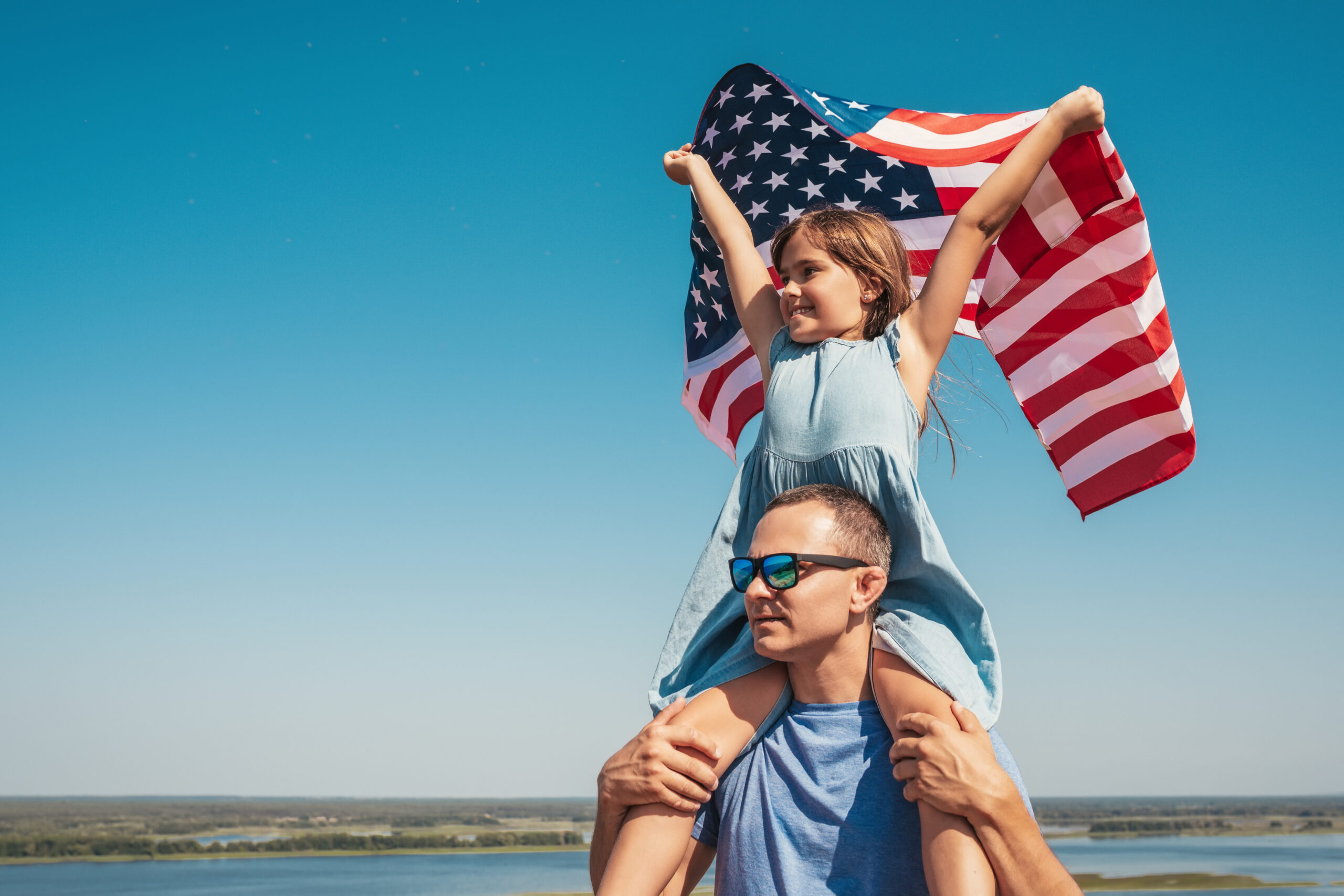 Girl with a US Flag on the shoulders of her father.