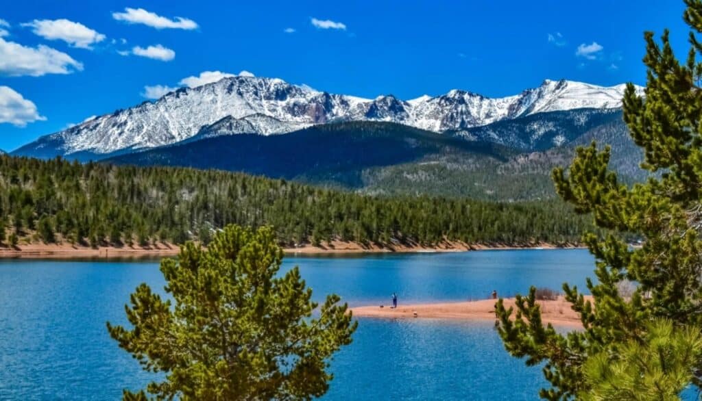 View of the Rocky Mountains with snow on the peaks. Surrounded by trees and the water.