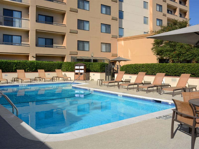 View of the outdoor pool surrounded by sun chairs, with the hotel behind.