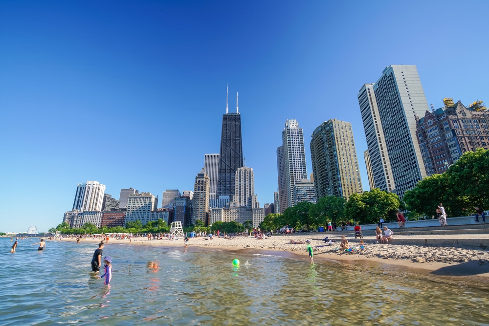 Families cool off at North Avenue Beach, where kids build sandcastles and splash in Lake Michigan with the skyline rising just behind them.