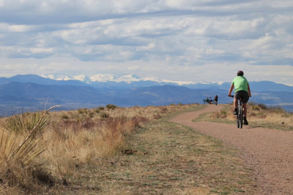 View of a cyclist riding on a trail with the mountains in the background.