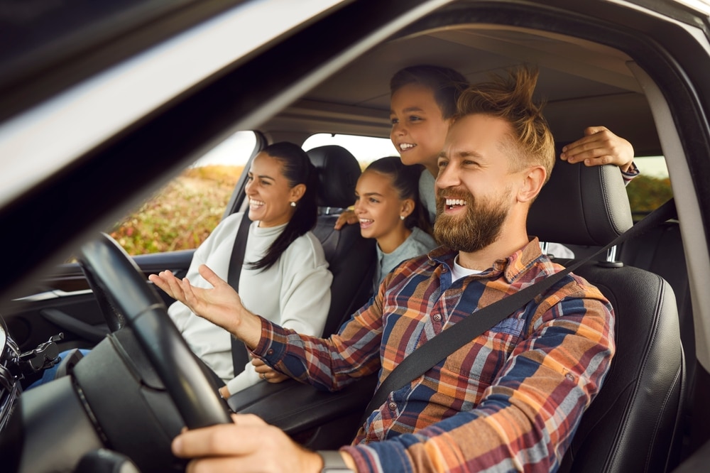 A family of four is happily driving in their car, enjoying a scenic view through the windows.