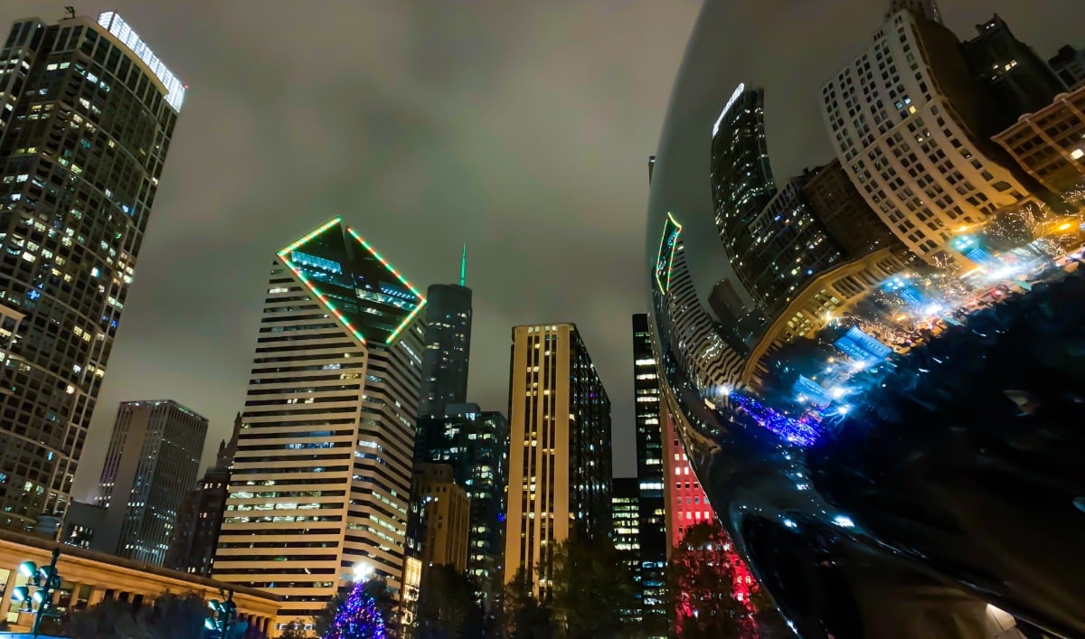 Chicago’s skyline reflected in Cloud Gate at night, with city lights and holiday colors illuminating Millennium Park