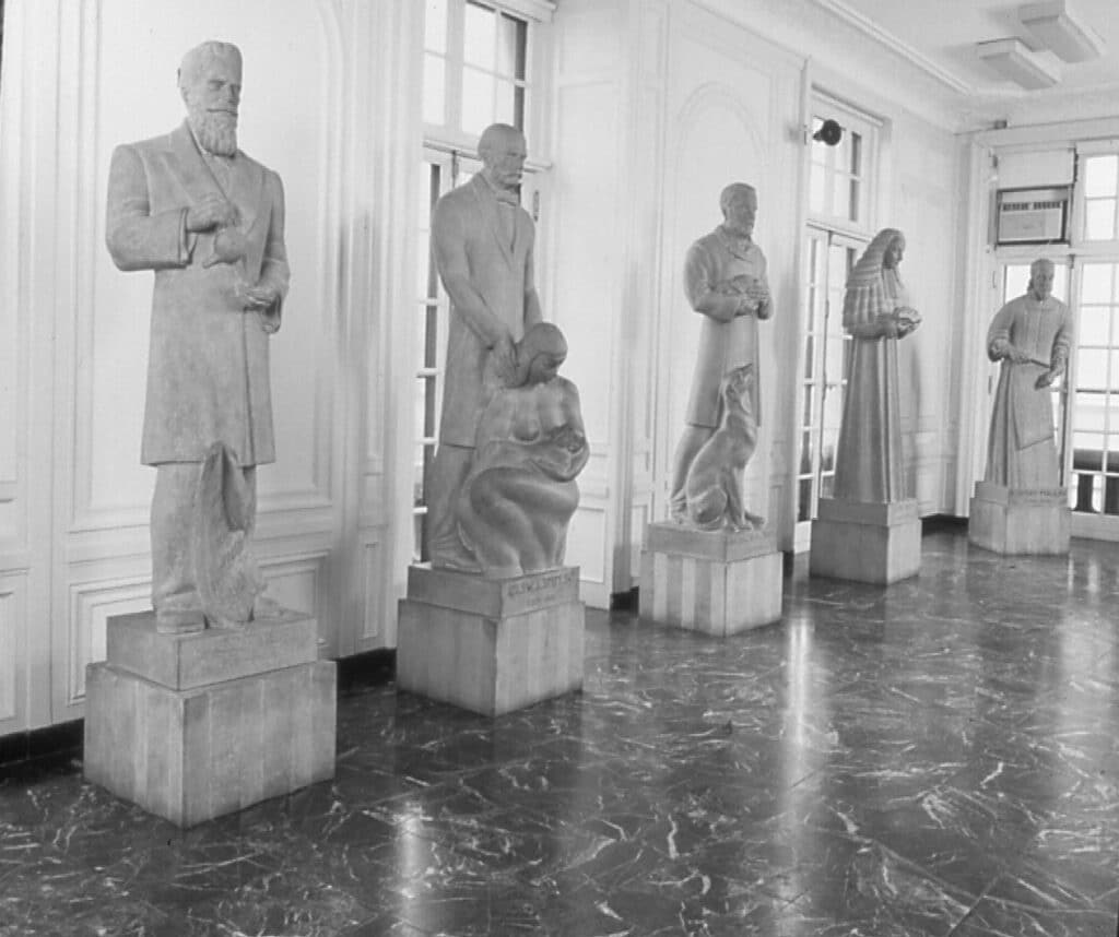 Black and white photo of several statues arranged in a spacious room, highlighting their intricate details and textures.