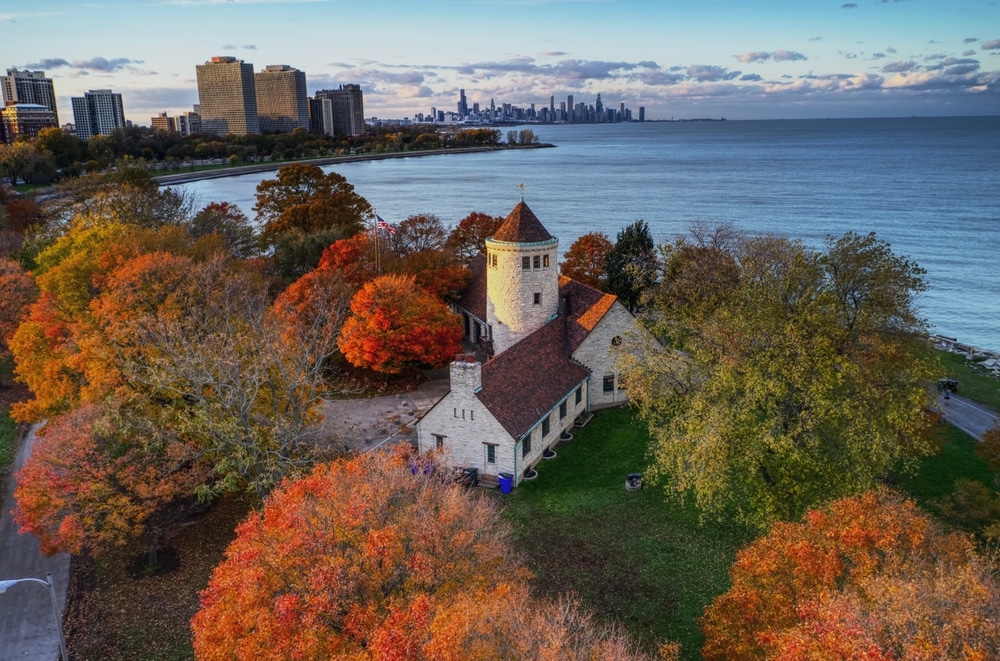 A field house surrounded by vibrant orange and red trees with views of the water in the back.