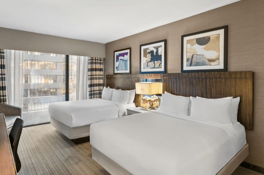 Two beds in a hotel room with a desk and a television positioned against the wall.