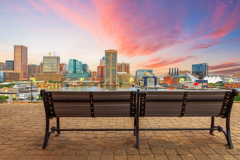 A bench on a brick walkway offers a view of the city skyline in the background.