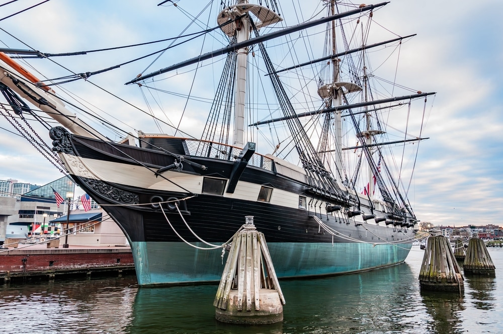 USS Constitution docked in Baltimore, Maryland, showcasing its historic wooden hull and sails against a clear blue sky.