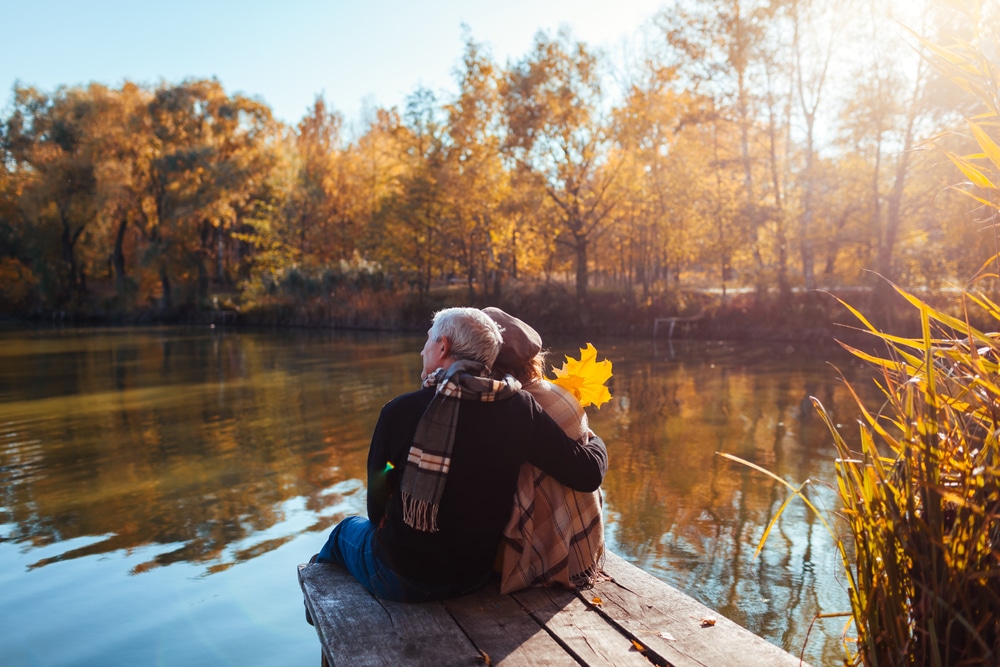 An older couple sits on a dock, gazing thoughtfully at the calm water in front of them.