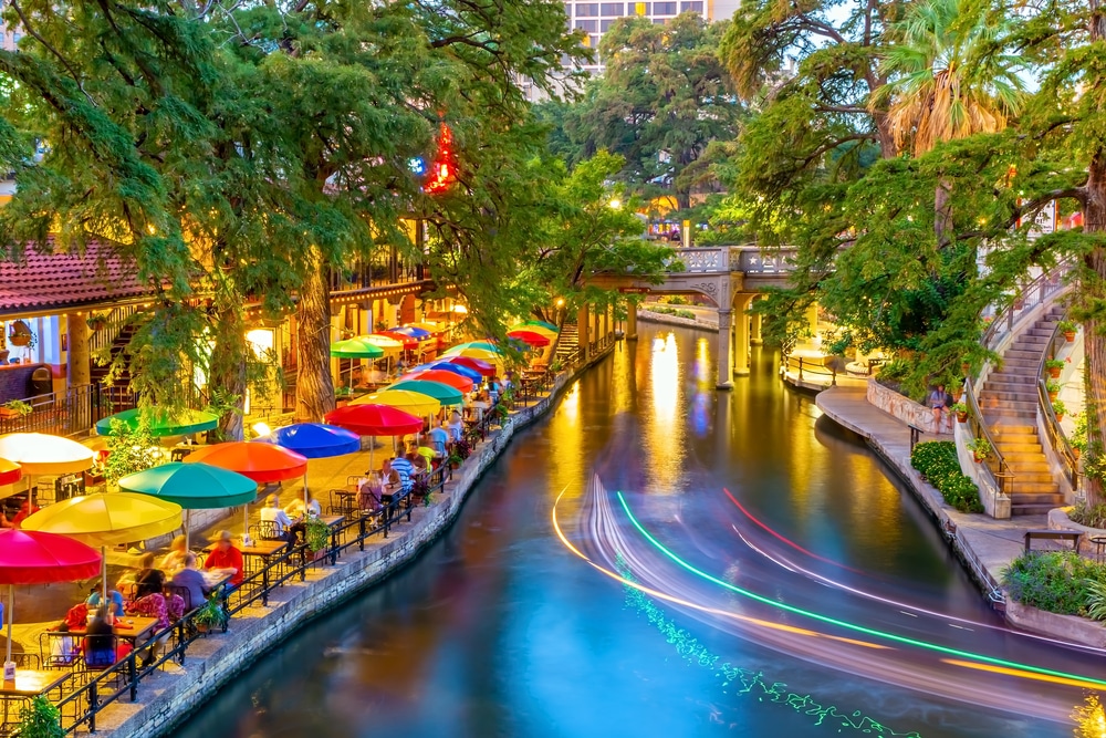 A scenic river lined with colorful umbrellas and tables, creating a vibrant outdoor dining atmosphere.