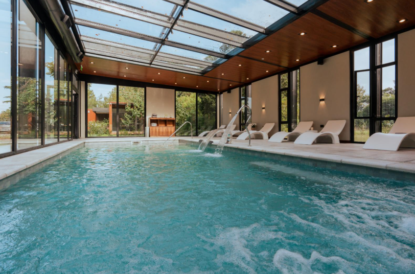 Indoor pool featuring lounge chairs and a glass roof, allowing natural light to illuminate the space.