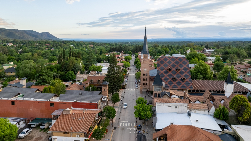 Aerial view of a town featuring a church surrounded by trees, showcasing the layout and greenery of the area.