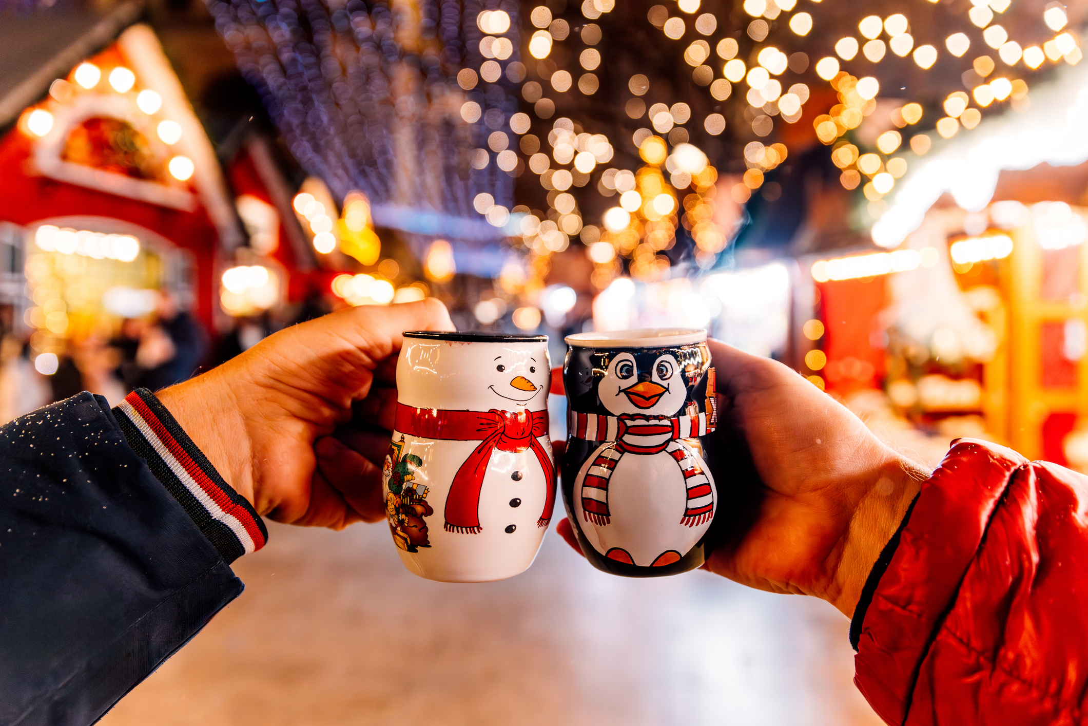 Two people smiling while holding mugs decorated with cheerful snowmen.