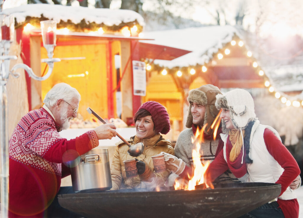 Three people are gathered around a fire pit, cooking food together outdoors.