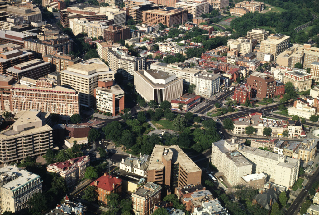 A sprawling cityscape featuring numerous buildings interspersed with lush green trees.