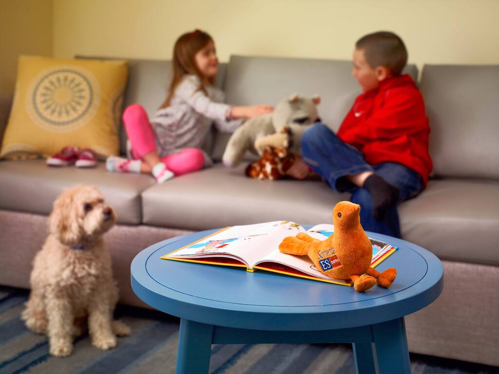 Two children joyfully playing with a stuffed animal in a bright, colorful room filled with toys.