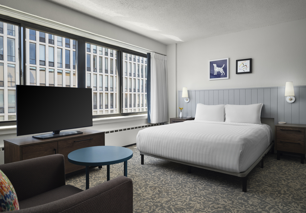 A hotel room featuring a neatly made bed, a television mounted on the wall, and a comfortable chair in the corner.