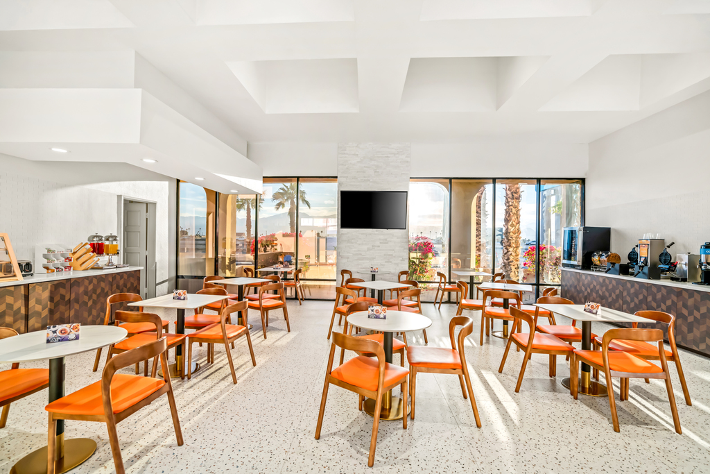 Hotel breakfast lobby showcasing a large open area with vibrant orange chairs and tables for dining.