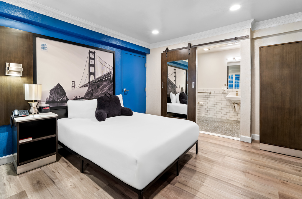 A hotel room featuring blue walls, a neatly made bed, and minimalistic decor for a calming atmosphere.