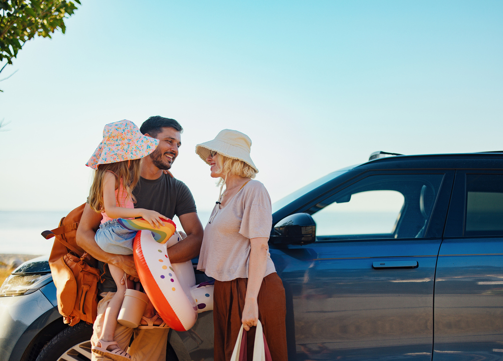 A family with a child stands beside a parked car, smiling and enjoying their time together outdoors.