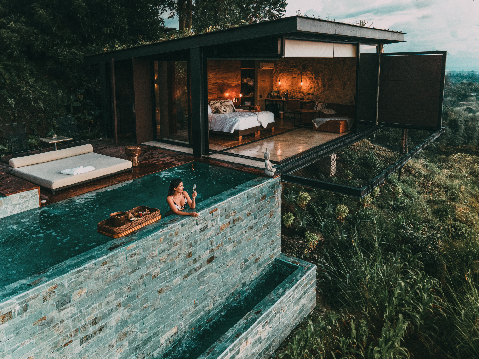 A scenic view of a luxury hotel, featuring lush gardens and a serene pool area under a clear blue sky.