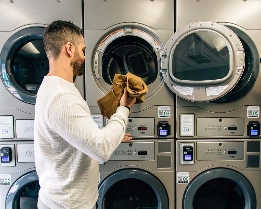 A man is seen placing his hand inside a washing machine, likely to take out freshly washed garments.
