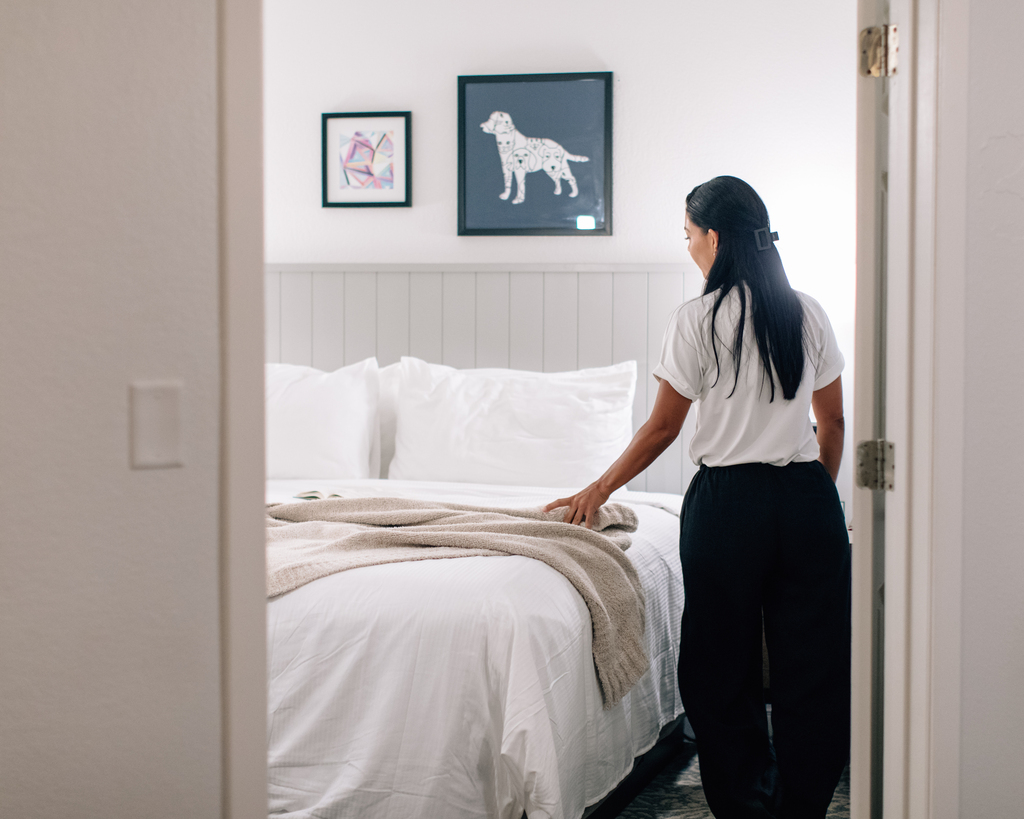A woman is positioned in front of a bed, with a dog image prominently featured on the wall behind her.