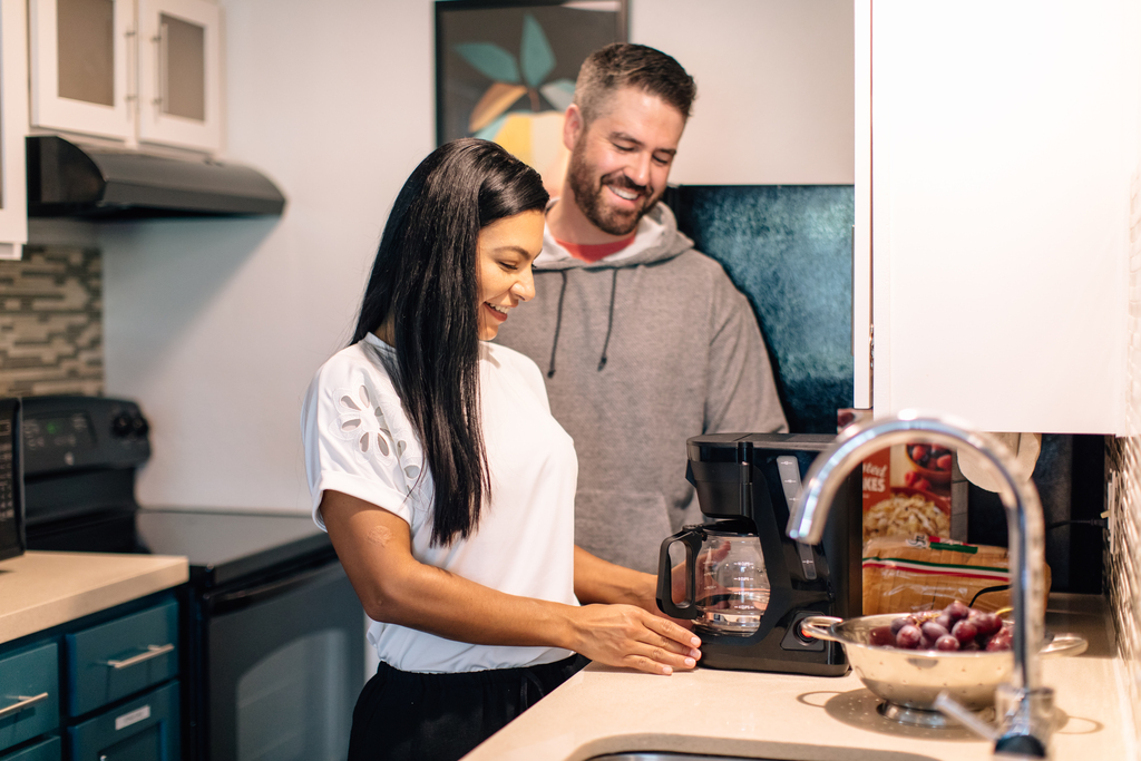 A man and woman are engaged in cooking in a kitchen, surrounded by fresh produce and cooking utensils.