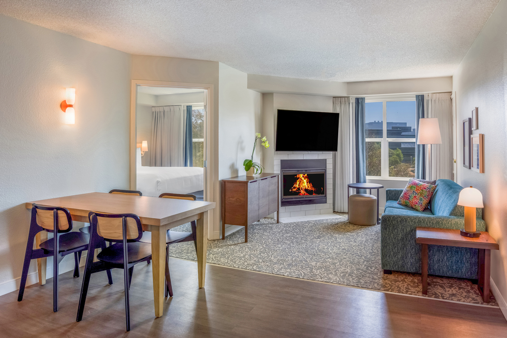 A cozy room featuring a comfortable couch, a wooden table, and a warm fireplace, creating an inviting atmosphere.