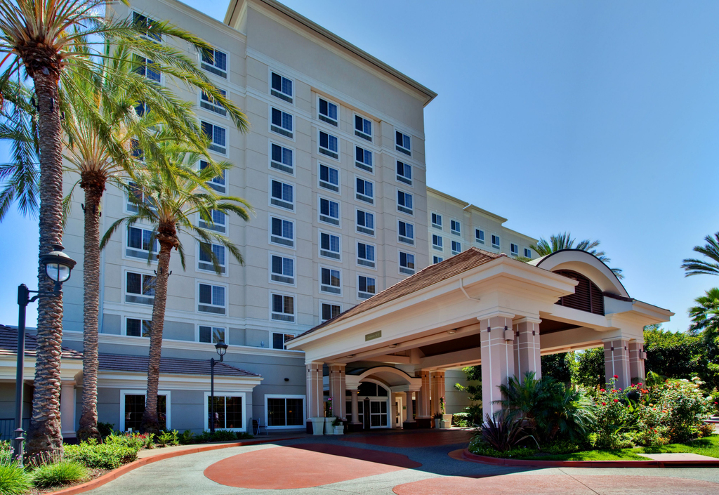 A stylish hotel entrance with a canopy, potted plants, and a prominent sign displaying the hotel's name.