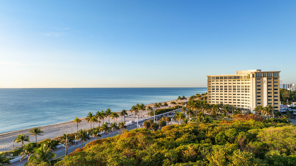 Aerial view of a beach with a hotel, showcasing sandy shores and turquoise waters.