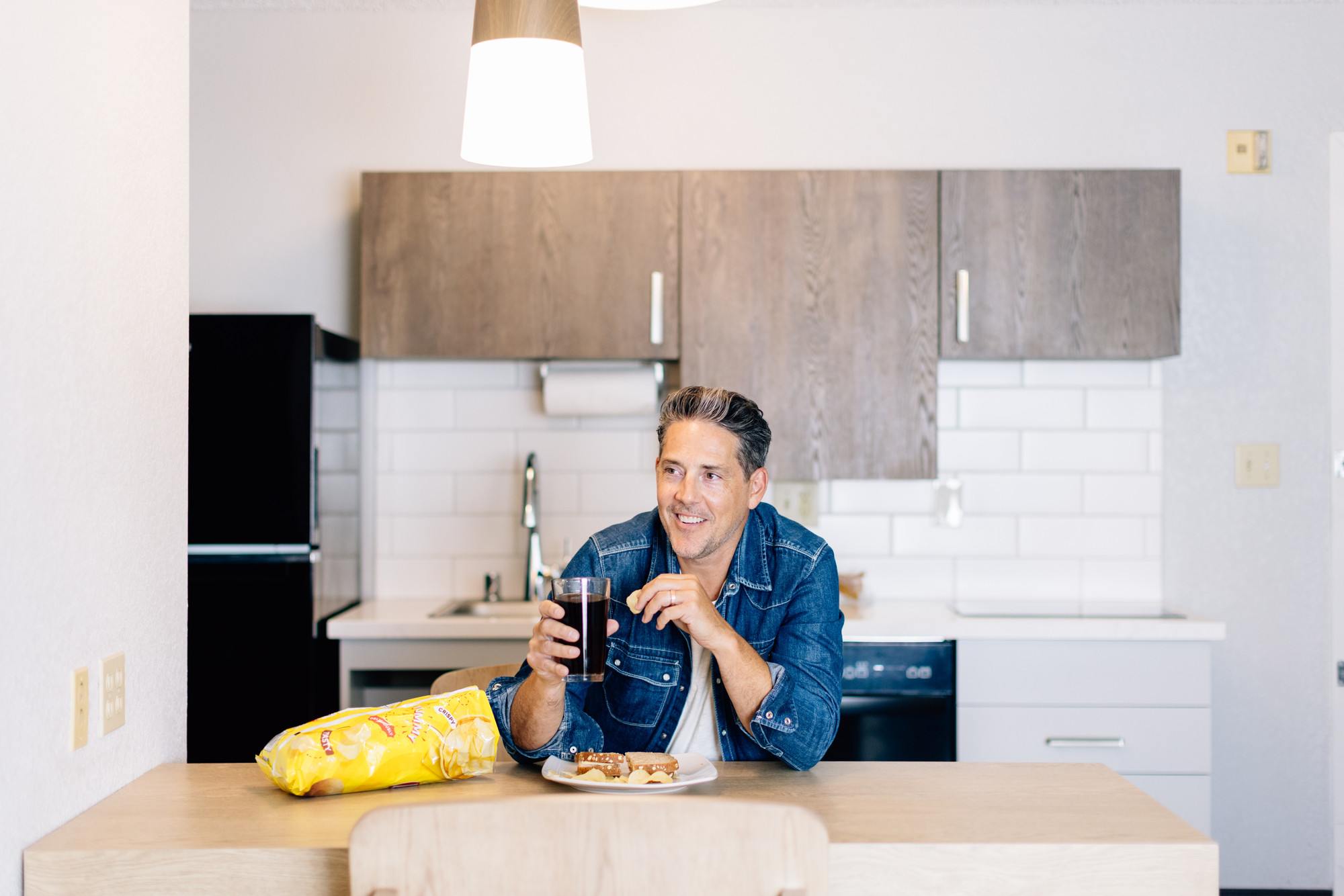 A man at a table, eating a sandwich while drinking a soda.