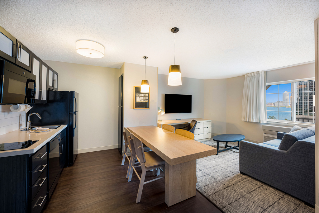 A compact hotel kitchen and living room featuring modern appliances and cozy furnishings.