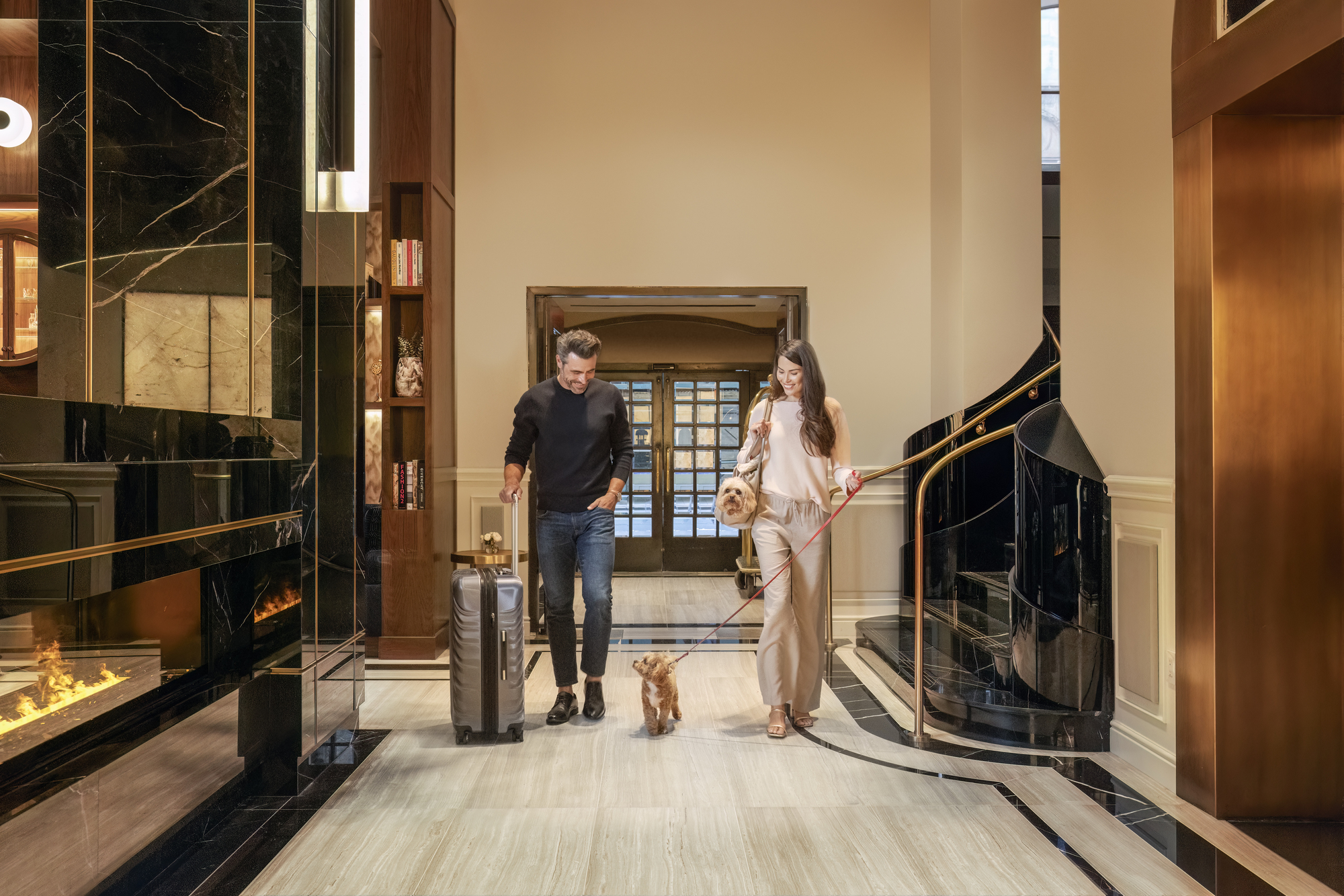 A man and woman walk together in a hallway, with a dog trotting ahead of them.