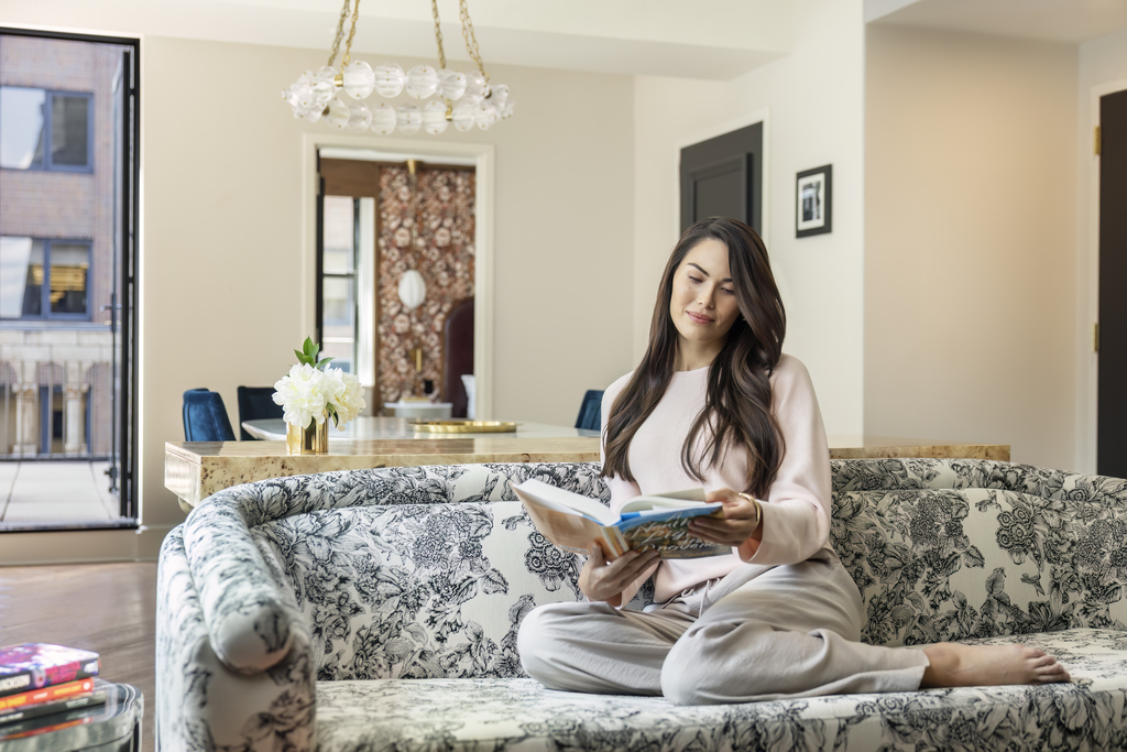 A woman is seated on a couch, deeply engaged in reading a book, surrounded by a comfortable setting.