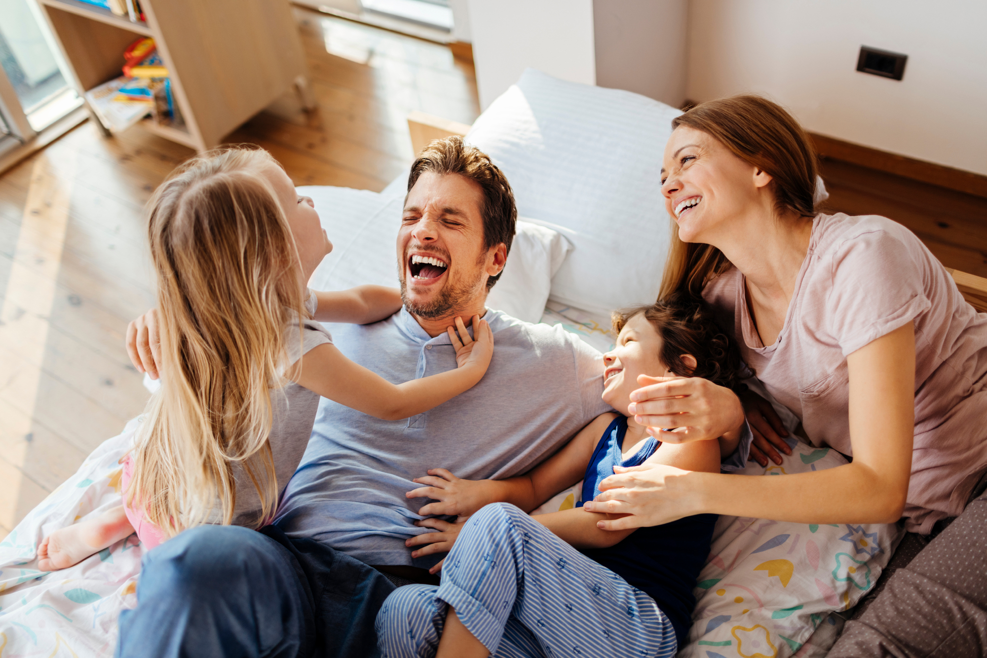 A family of four joyfully laughing together on a bed, creating a warm and playful atmosphere.