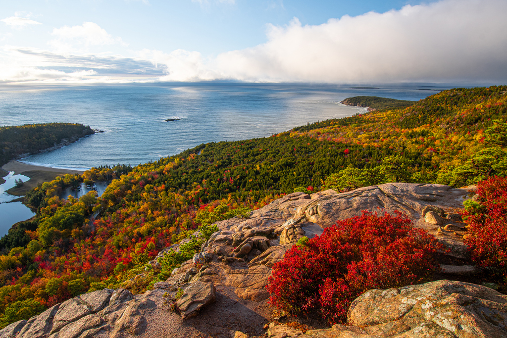 A scenic view of a rocky area leading to a tranquil body of water in the background, surrounded by natural beauty.