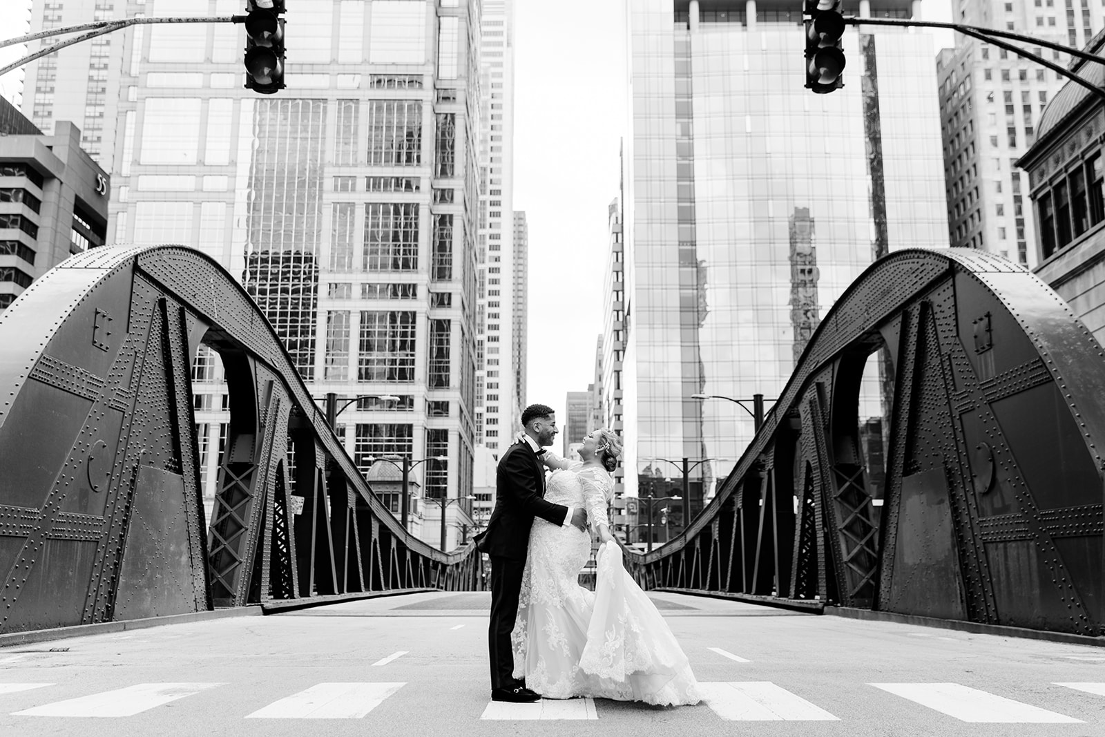 A black and white photograph of a bride and groom standing on a bridge.