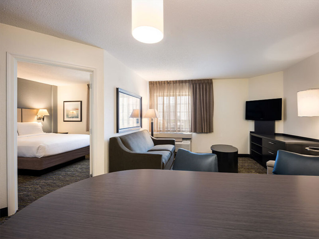 A hotel room featuring a neatly made bed, a comfortable couch, and a flat-screen television on the wall.