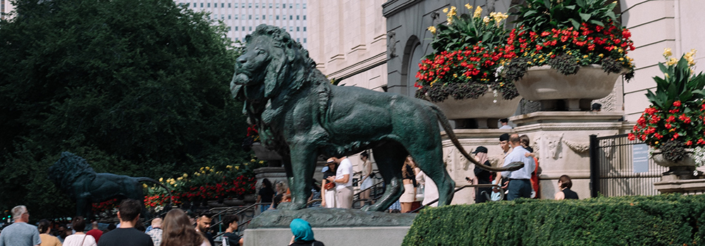 A group of five people poses in front of a large lion statue in a public park.