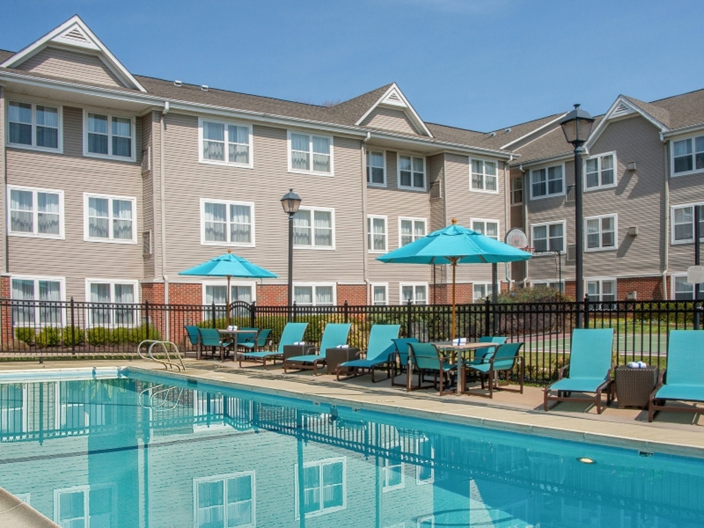 A pool surrounded by lounge chairs and greenery in an urban setting.