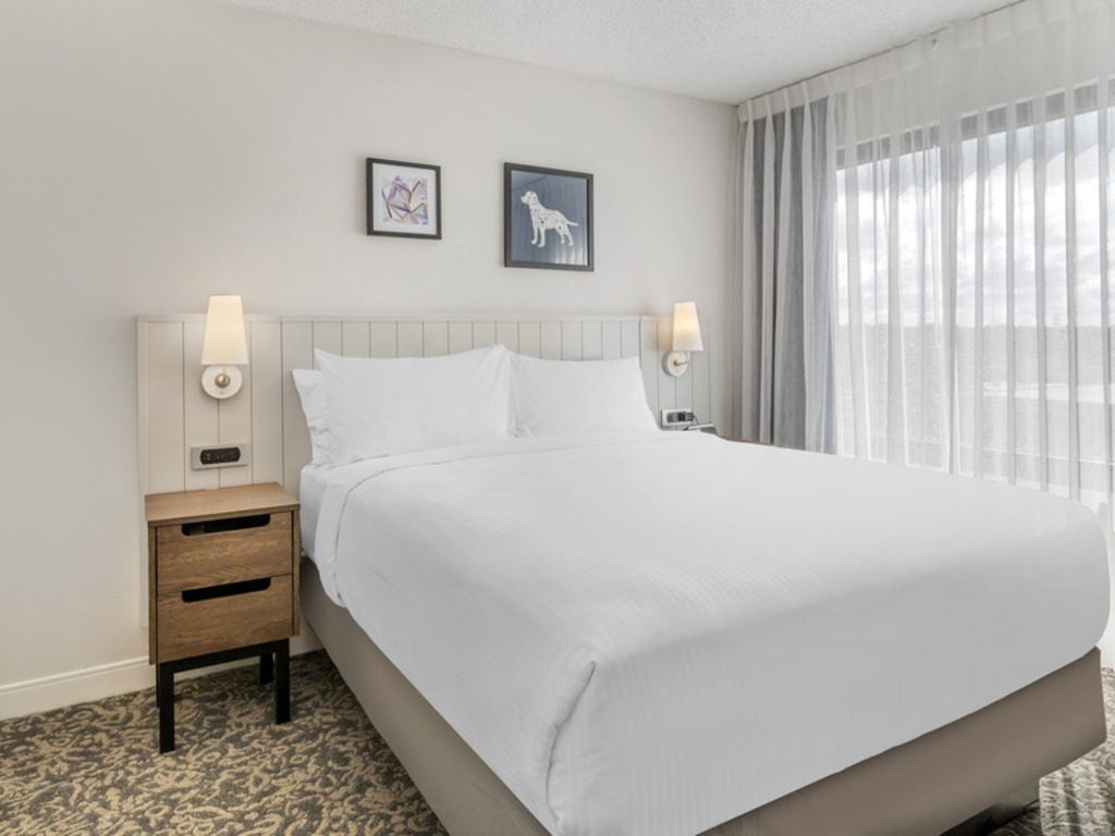 A hotel room featuring a neatly made bed and a large window allowing natural light to enter.