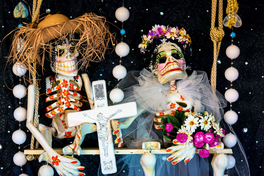 Two skeletons hold a cross and a bouquet of flowers.