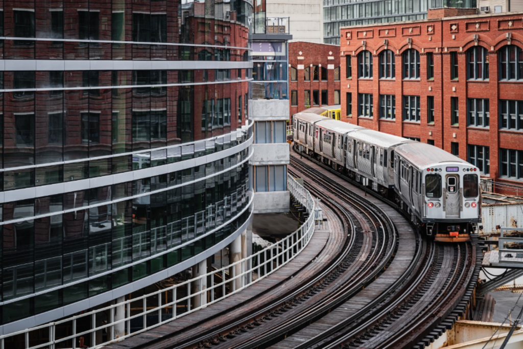 A train moves along tracks through an urban landscape, with buildings visible in the background.