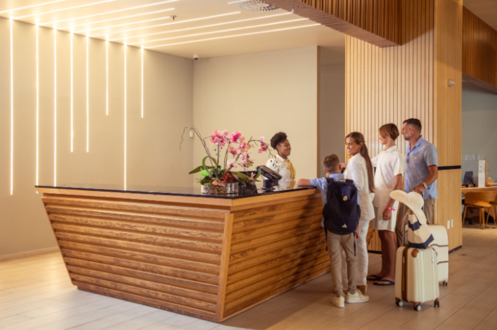 A family of four stands at the hotel front desk, interacting with the receptionist and checking in.