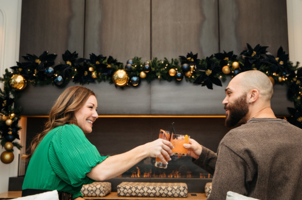 A couple clinks glasses in front of a cozy fireplace, celebrating a special moment together.