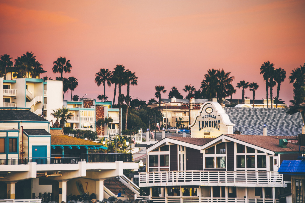 A scenic view of the ocean and buildings silhouetted against a vibrant sunset sky.