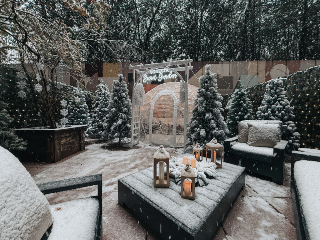 Snow-covered outdoor patio featuring a cozy fireplace and several chairs arranged for seating.