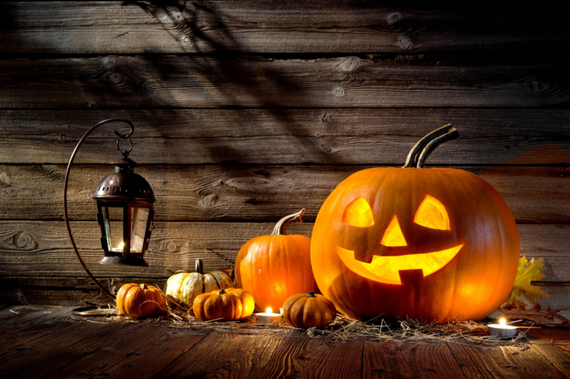 A carved Halloween pumpkin sits on a wooden background, showcasing intricate designs and a warm glow from within.