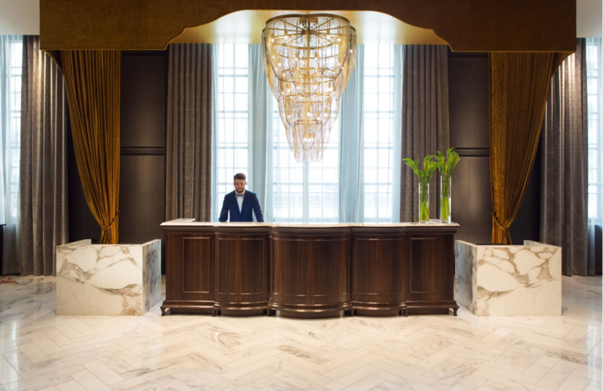 A luxurious hotel lobby featuring elegant marble floors and a grand chandelier overhead.